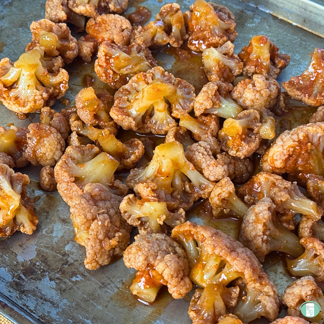 Cauliflower pieces in sauce on cooking sheet.
