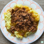 shredded beef and sauce over mashed potatoes on a plate