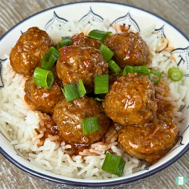 meatballs in sauce on rice in a bowl topped with sliced green onions