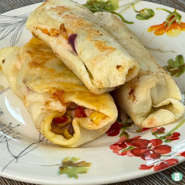Three baked chicken burritos on flower plate.