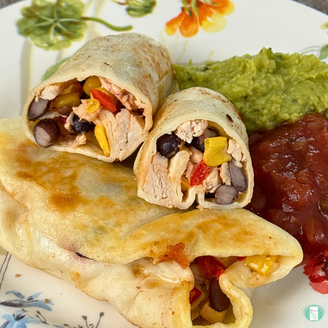 Burritos with chicken, corn and beans with guacamole and salsa on plate.