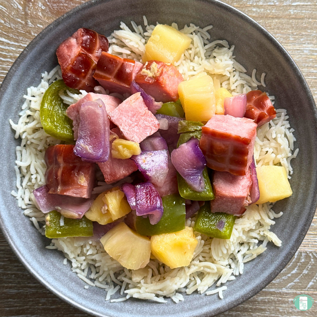 Cooked ham, green pepper, purple onion and pineapple served with rice in bowl.