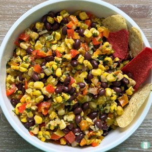 kernel corn, black beans, red peppers, and cilantro in a bowl with some tortilla chips