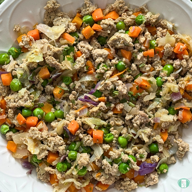Cooked ground turkey, carrots, peas, onions in white bowl.