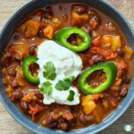 bowl of sweet potato and bean chili topped with sour cream, cilantro, and jalapeno slices