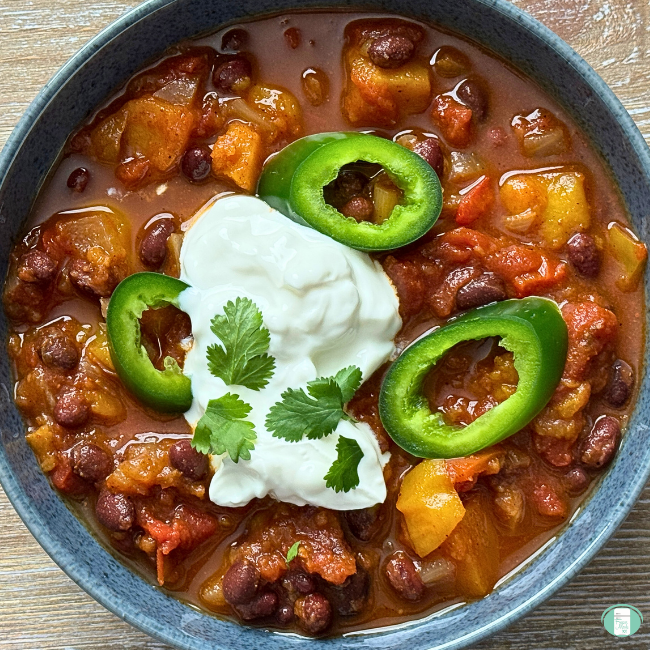 bowl of sweet potato and bean chili topped with sour cream, cilantro, and jalapeno slices