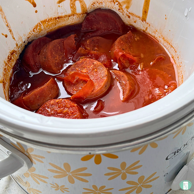Kielbasa sausage cut up and cooking in a ketchup, horseradish, and brown sugar sauce inside a crock pot