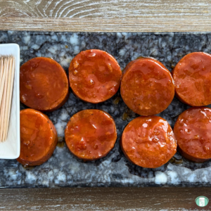 Candied kielbasa bites made of garlic sausage coated in a sweet and tangy sauce, served on a platter with toothpicks