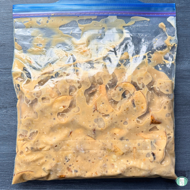 Meatballs covered in a light orange creamy mushroom stroganoff sauce inside of a large freezer ziploc bag