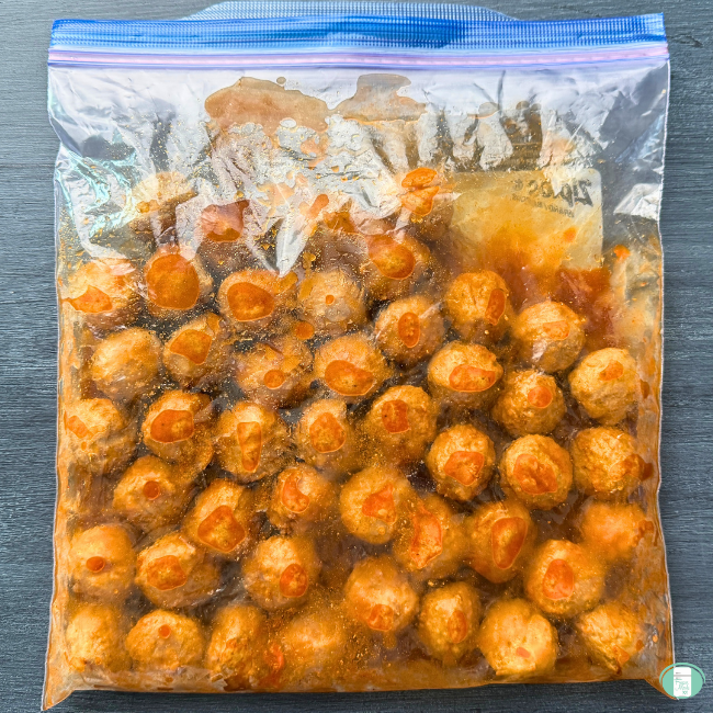 Freezer meal meatballs in a ziploc bag with sweet and spicy sauce covering them