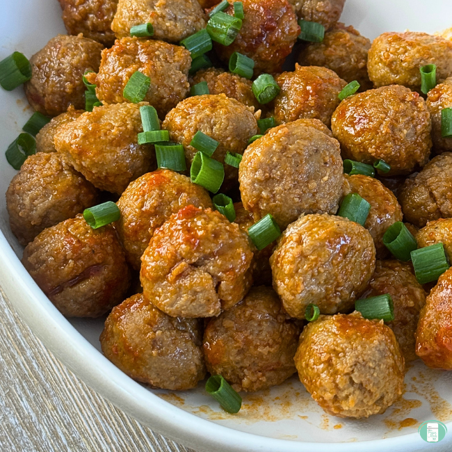 Slow cooker sweet and spicy meatballs smothered in sauce, served with green onions in a big white bowl