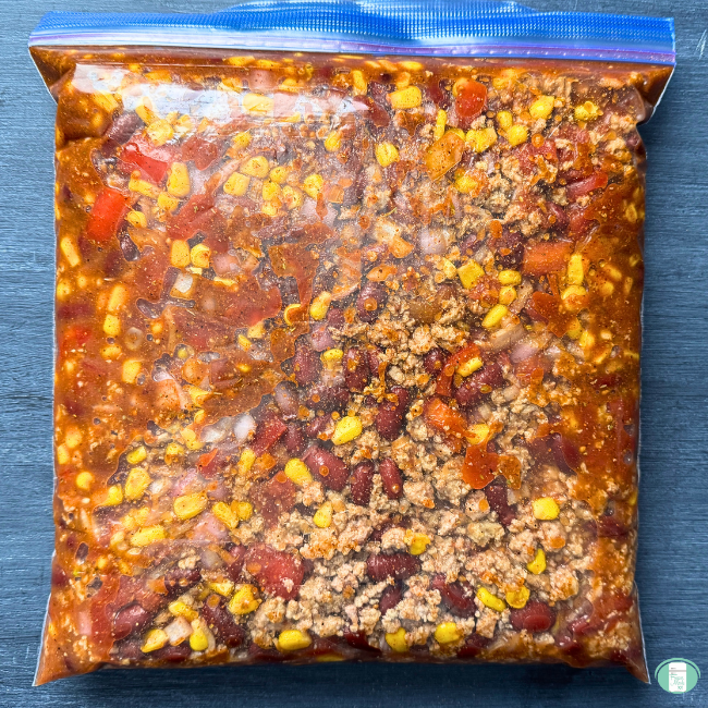 Turkey chili in a ziploc freezer bag, showing ground turkey, tomatoes, corn, ground turkey, beans, and seasonings