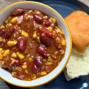 Slow cooker turkey chili with beans, ground turkey, corn, and more served in a bowl with a white bun on the side