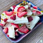 Freezer friendly healthy snack of frozen yogurt bark with strawberries, raspberries, and pistachios served on a blue plate
