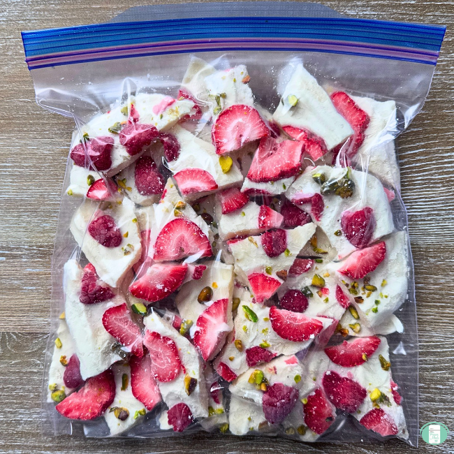 Chunks of frozen yogurt bark broken up in a ziploc bag, with yogurt, strawberries, raspberries, and pistachios frozen into sweetened yogurt