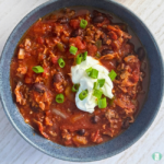 Freezer meal low carb chili with beans, ground beef, bacon, jalapenos, and more, served in a bowl with sour cream and green onion on top