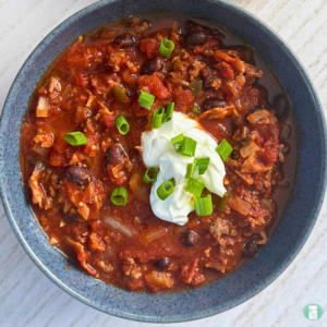 Freezer meal low carb chili with beans, ground beef, bacon, jalapenos, and more, served in a bowl with sour cream and green onion on top