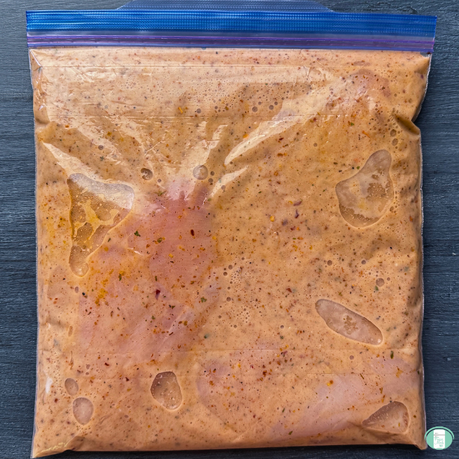 Cajun chicken alfredo in a ziploc bag ready to go in the freezer, with chicken breast and a well-seasoned orange sauce coating it