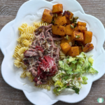 Freezer meal sweet roasted butternut squash served on a plate with salad, pasta, and meat