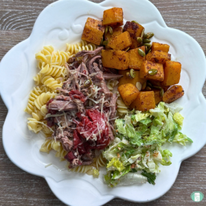 Freezer meal sweet roasted butternut squash served on a plate with salad, pasta, and meat