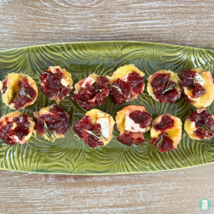 Freezer-friendly cranberry brie bites appetizer with sprigs of fresh rosemary on top, served on a green plate