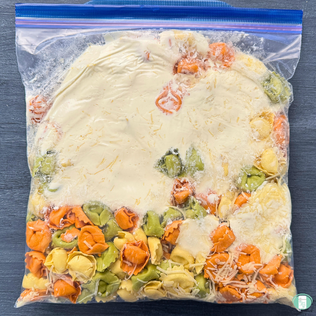 Crockpot tuscan chicken tortellini meal in a ziploc bag, prepped to go in the freezer, with cheese, tortellini, and more