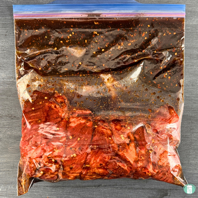 Make ahead Korean beef tacos in a ziploc bag ready to be frozen, showing beef chuck roast and a dark red sauce with red pepper flakes