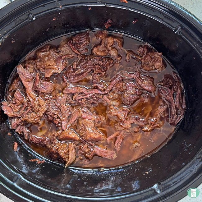 Korean Beef Tacos cooking in the slow cooker, with shredded beef chuck roast in a rich sauce