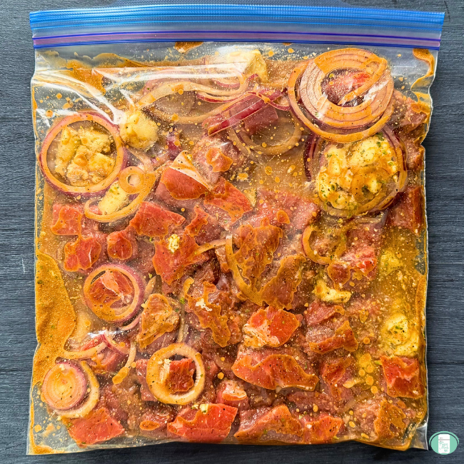 Slow cooker steak bites in a ziploc to be frozen, with cubed steak, seasonings, and onion