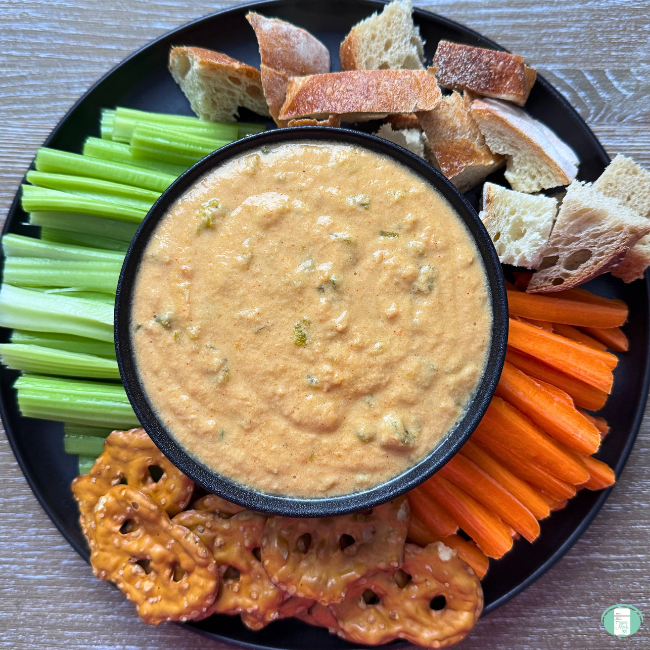 Spicy slow cooker queso served in a bowl with bread, pretzels, and vegetables to dip