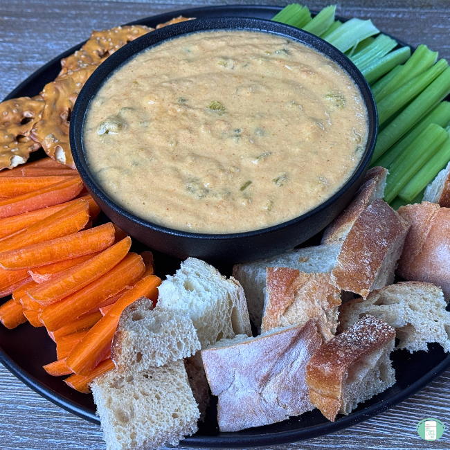 Make ahead spicy slow cooker queso served in a bowl with carrots, celery, bread, and pretzels to dip