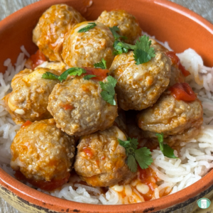 Freezer meal enchilada meatballs with red sauce, melted cheese, and cilantro garnish, served on rice