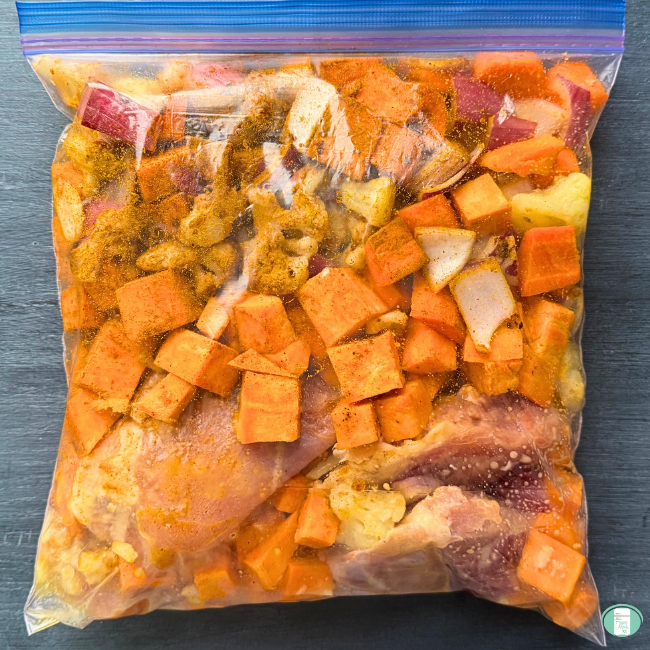 Freezer meal moroccan chicken sheet pan prepped in a ziploc for freezing, with chicken, cauliflower, purple onion, sweet potato, carrots, and seasoning