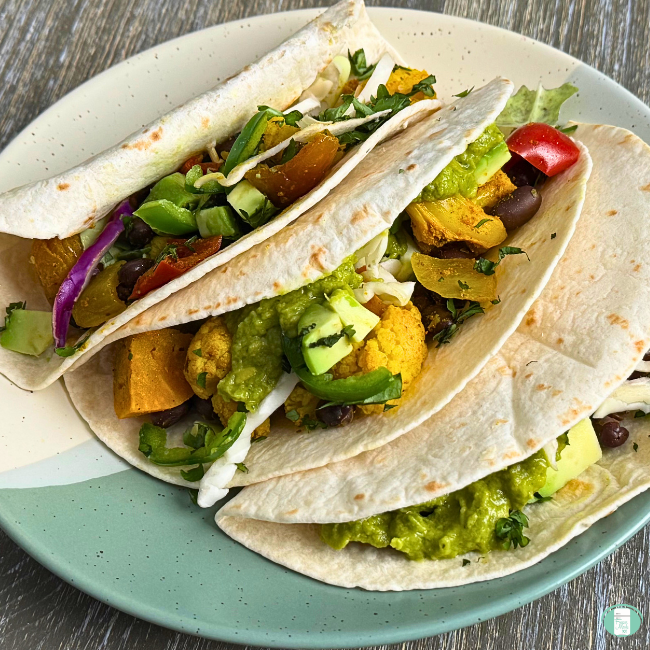 Make ahead vegetarian roasted veggie tacos with cauliflower, beans, peppers, avocado, coleslaw, and sweet potatoes served in mini tortillas